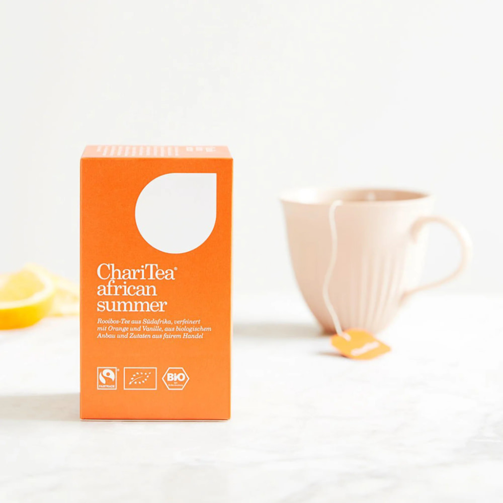 Tee in oranger Verpackung und eine Tasse mit Tee auf hellem Hintergrund.