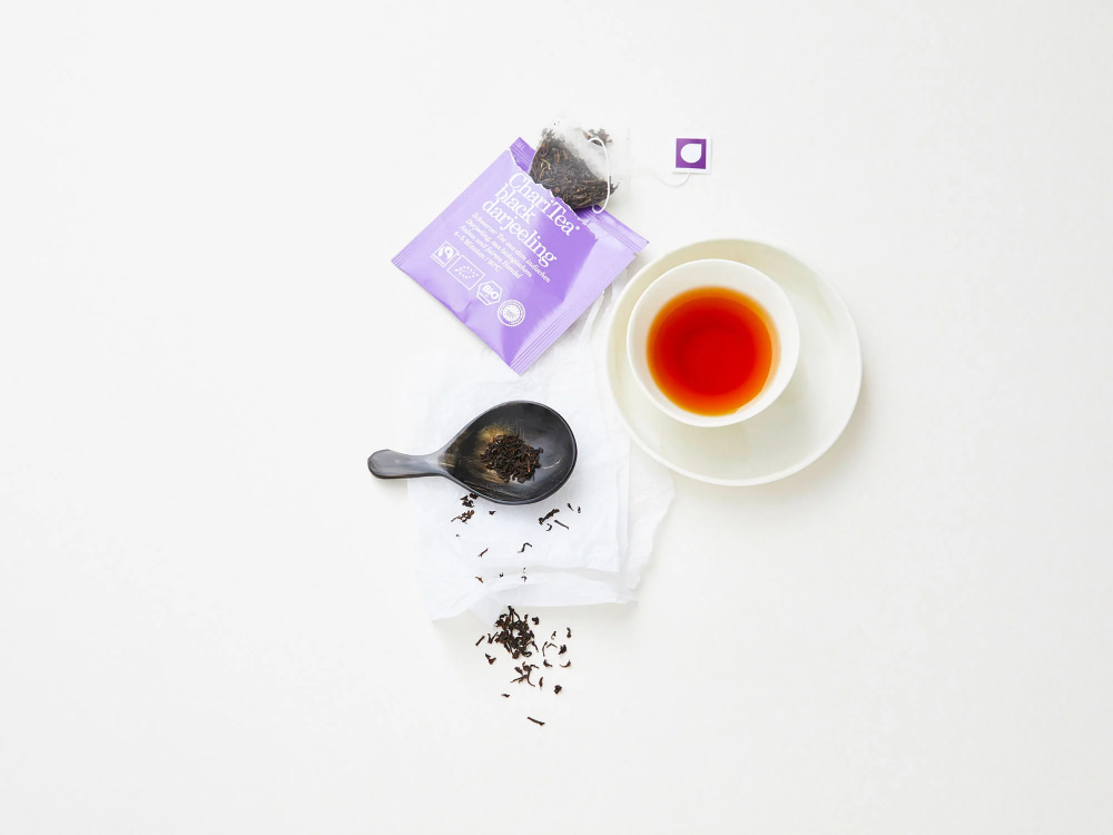 Geöffnete Teepackung mit Glas Tee und Tee auf Löffel auf hellem Hintergrund.