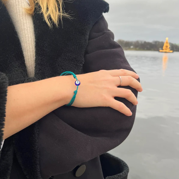 Junge Frau mit türkisfarbenem Upcycling-Armband am Handgelenk, See im Hintergrund