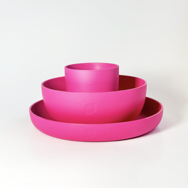 Plastikgeschirr-Set bestehend aus Teller, Schälchen und Becher in Pink auf weißem Hintergrund.