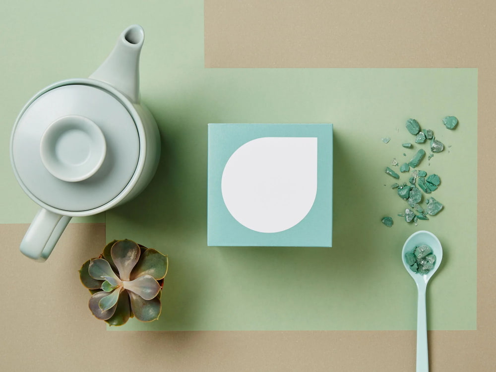 Tee in mintfarbener Verpackung, Teekanne, Blume und Löffel auf mintfarbenem Hintergrund