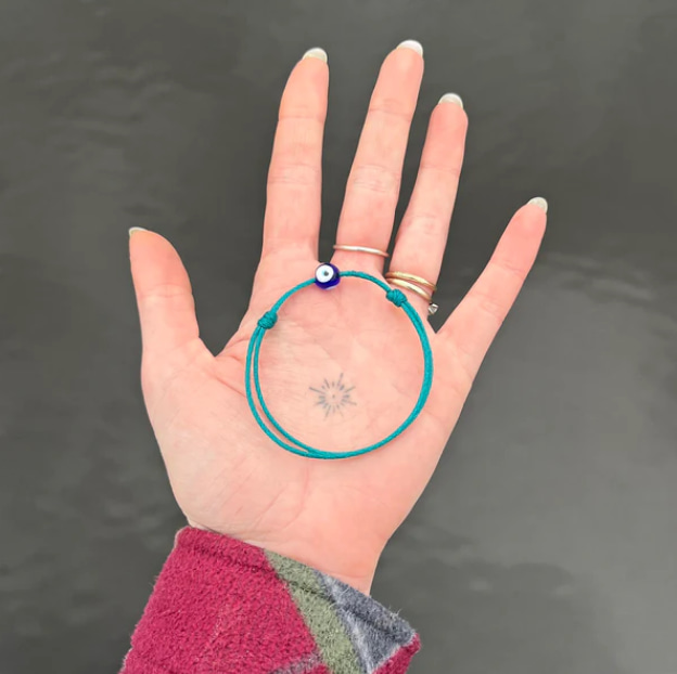 Eine Hand mit einem türkisfarbenen Upcycling-Armband auf grauem Hintergrund.