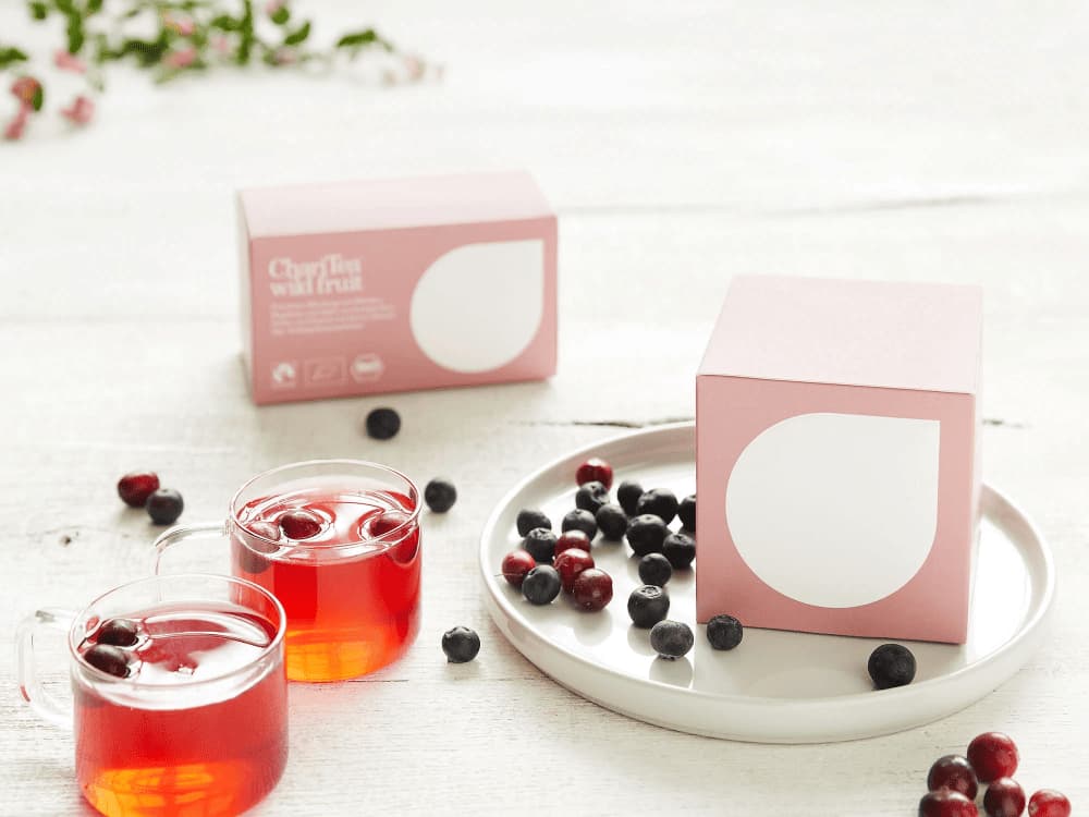 Zwei Gläser Tee, Teeverpackung auf Teller und frische Wildbeeren